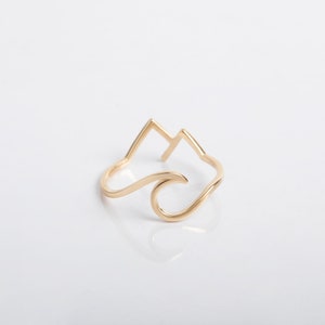 May include: A gold ring with a wave and mountain design. The ring is made of a thin metal and is a simple, minimalist design.