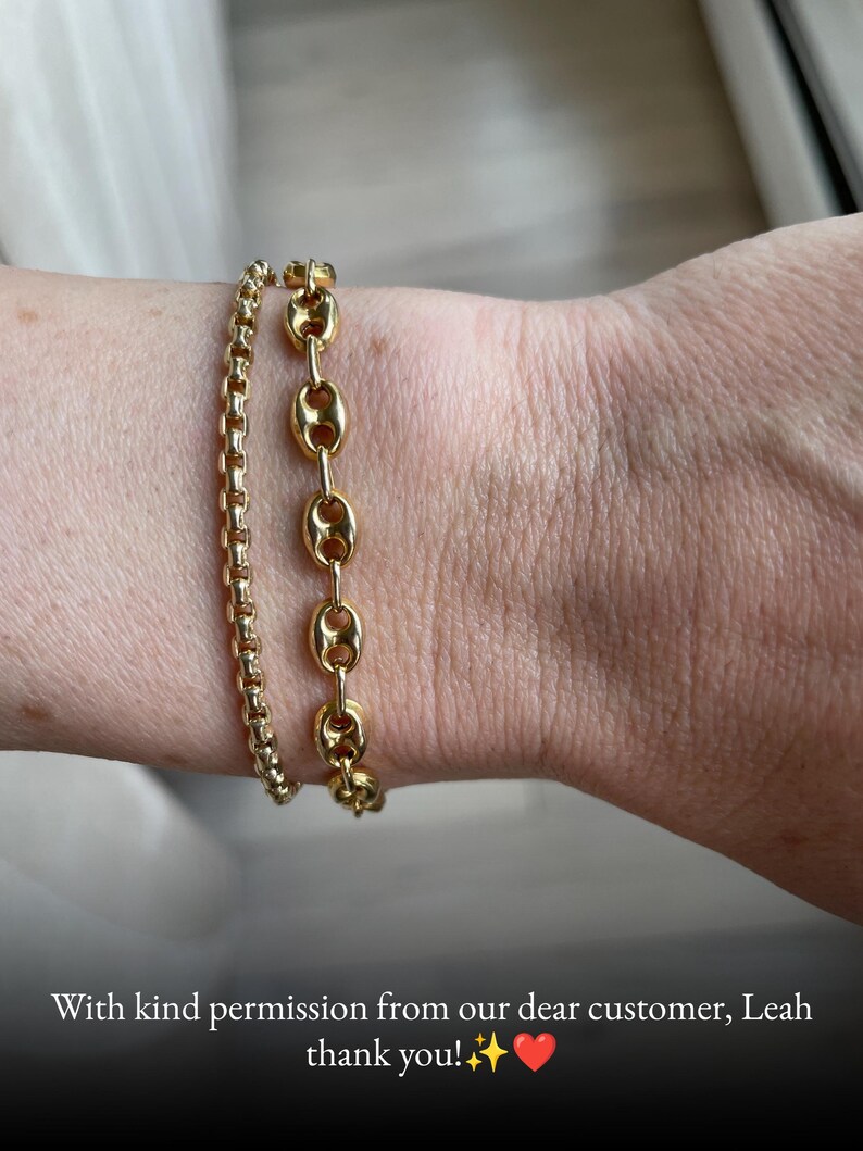 May include: Two gold-toned bracelets worn together. One bracelet features a delicate, rounded box chain design, while the other consists of larger, oval-shaped links with a central bar, creating a layered look on the wrist.