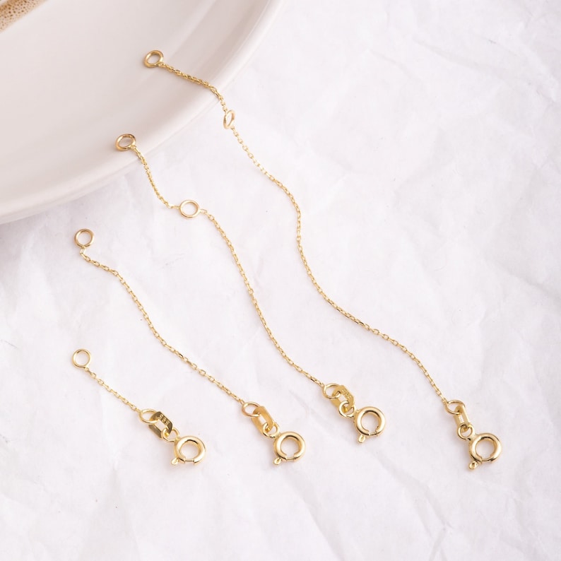 May include: Four gold chain extenders of different lengths, each with a lobster clasp closure.