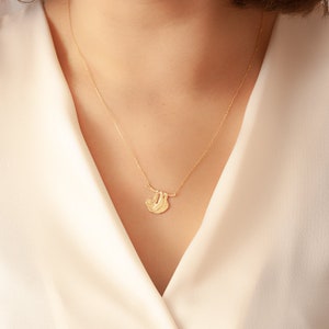 Pode incluir: Um colar de ouro com um pingente de pregui&ccedil;a pendurado em um galho. A pregui&ccedil;a est&aacute; virada para a esquerda e tem um design detalhado.