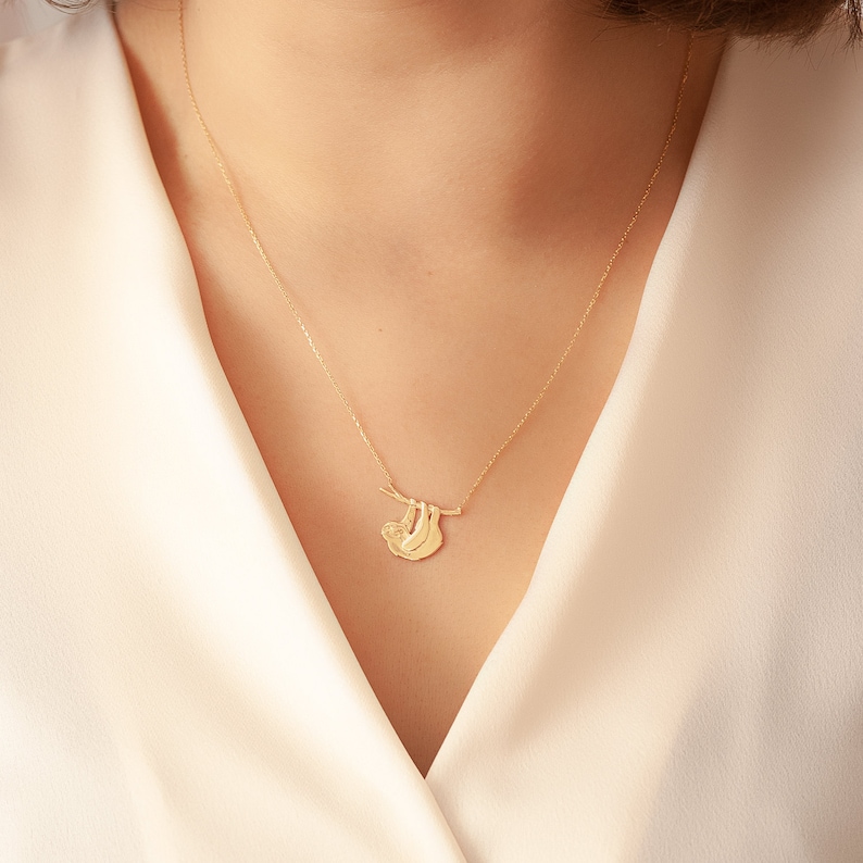 Pode incluir: Um colar de ouro com um pingente de pregui&ccedil;a pendurado em um galho. A pregui&ccedil;a est&aacute; virada para a esquerda e tem um design detalhado.