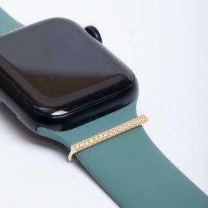 May include: A teal silicone watch band with a gold bar adorned with clear rhinestones.