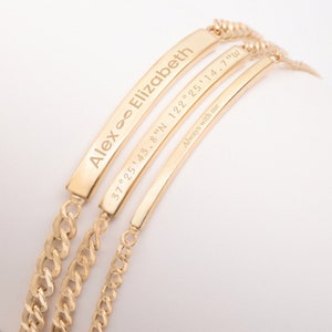 May include: Three gold bracelets with engraved text. The top bracelet reads "Alex ∞ Elizabeth". The middle bracelet reads "37°25'43.8"N 122°25'14.7"W". The bottom bracelet reads "Always with me".