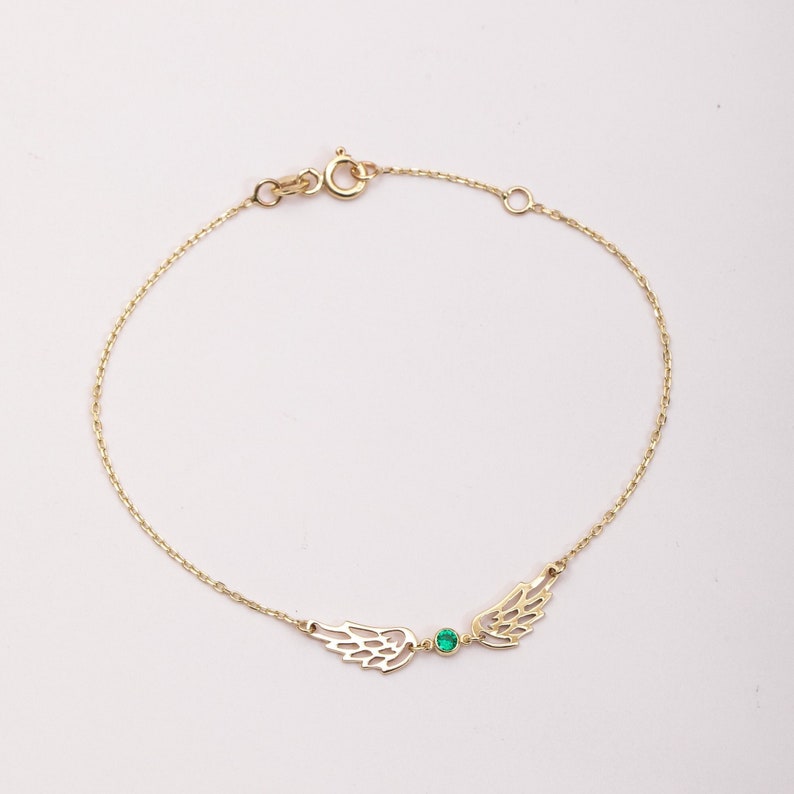 Puede incluir: Delicada pulsera de oro con dise&ntilde;os de alas caladas a ambos lados de una peque&ntilde;a gema verde redonda. La pulsera tiene una fina cadena y un cierre de broche. Una pieza de joyer&iacute;a sencilla y elegante.