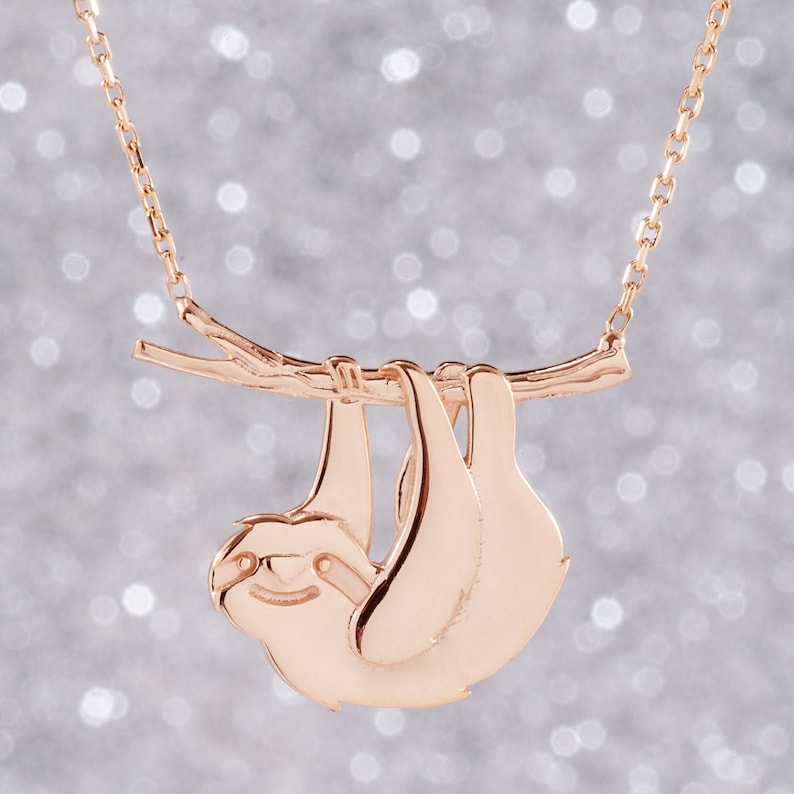 Pode incluir: Um colar de ouro rosa com um pingente de pregui&ccedil;a pendurado em um galho. A pregui&ccedil;a &eacute; feita de metal e tem um design detalhado.