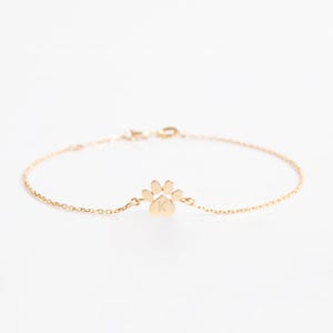 May include: A gold chain bracelet with a paw print charm featuring the letter K.