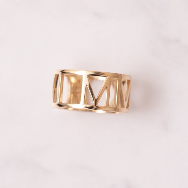 Pode incluir: Um anel dourado com um design de algarismos romanos. O anel &eacute; feito de metal e tem um design simples e elegante.