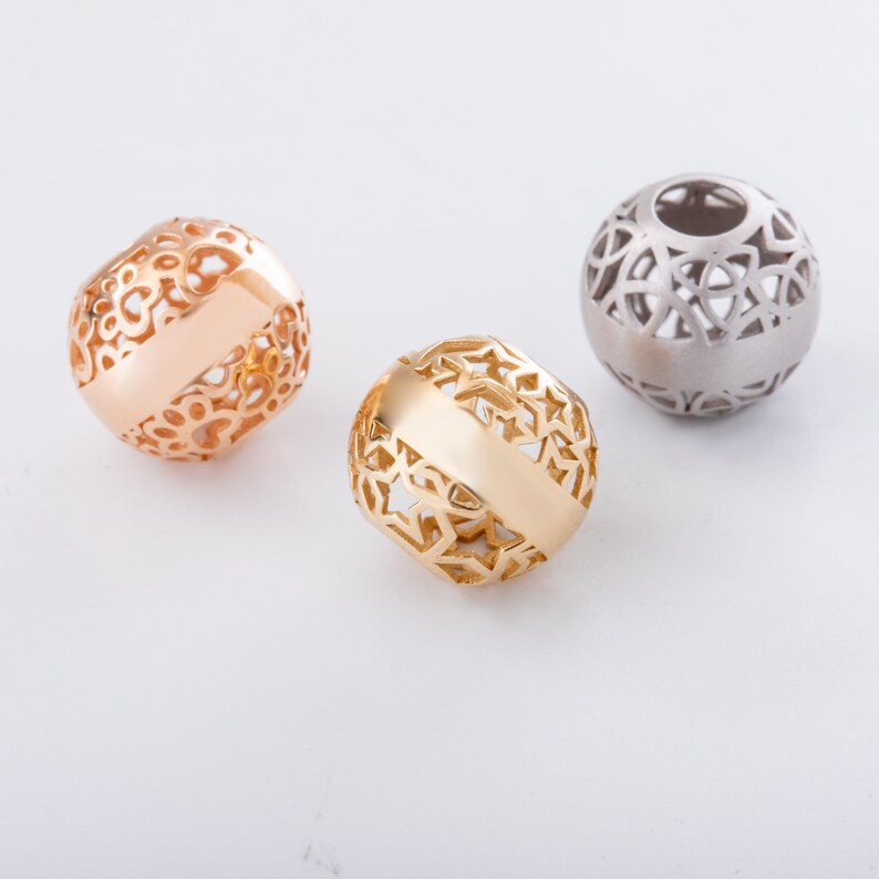 May include: Three decorative metal beads with intricate designs. The beads are gold, rose gold, and silver.