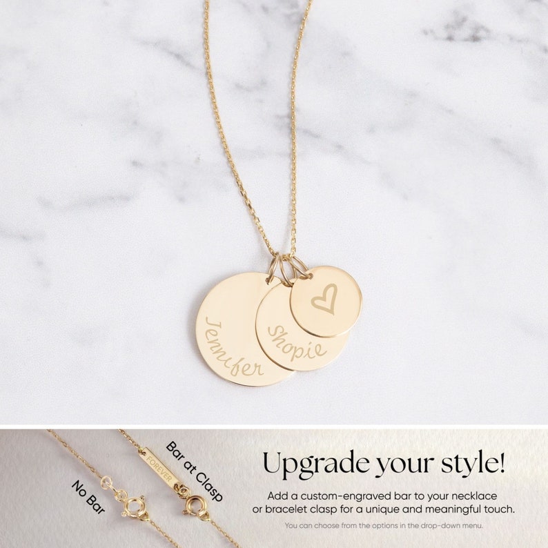 May include: Gold-colored necklace with three circular pendants. Two pendants are engraved with names, and the third has a heart symbol. The necklace is displayed on a marble surface. The image also shows clasp options.