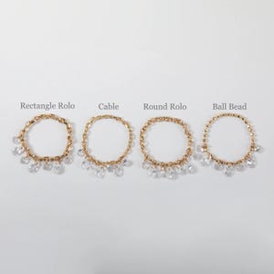 May include: Four gold-toned metal chains arranged in a row, each featuring dangling clear teardrop-shaped charms. The chains are labeled Rectangle Rolo, Cable, Round Rolo, and Ball Bead, showcasing distinct link styles for each jewelry piece.