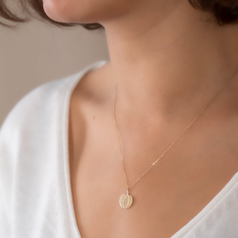 Puede incluir: Un collar de oro con un delicado colgante geom&eacute;trico con forma de calabaza. El colgante tiene un dise&ntilde;o texturizado y en capas.