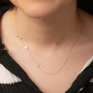 Puede incluir: Un collar de cadena de oro con un pequeño dije de flor y un dije de la letra 'U'.