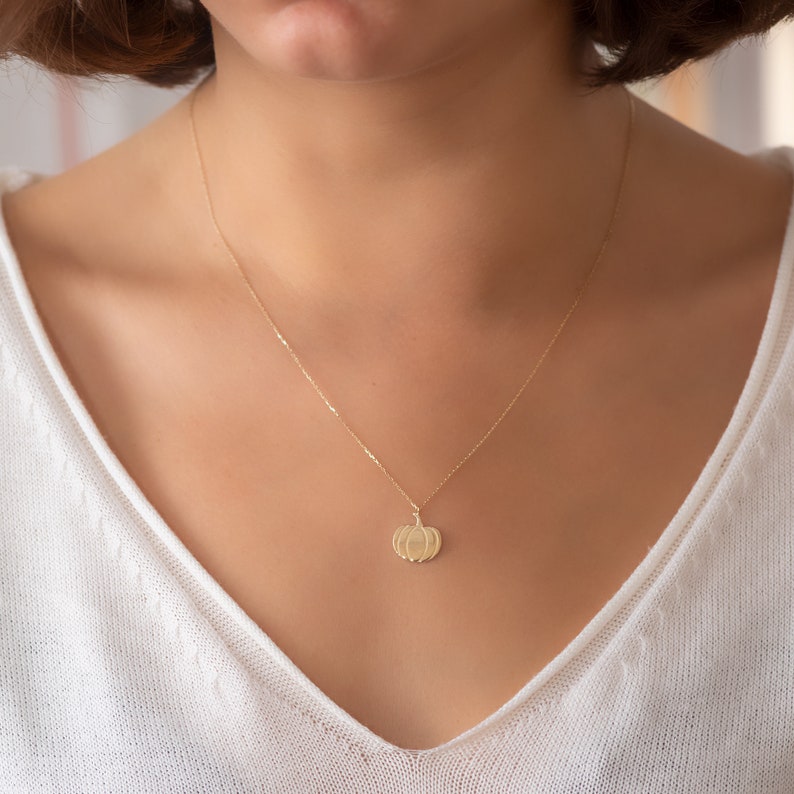 Puede incluir: Un collar de cadena de oro con un peque&ntilde;o colgante de calabaza.