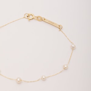 Puede incluir: Un brazalete de cadena dorada con cinco pequeñas perlas blancas y una etiqueta que dice "LOVE".