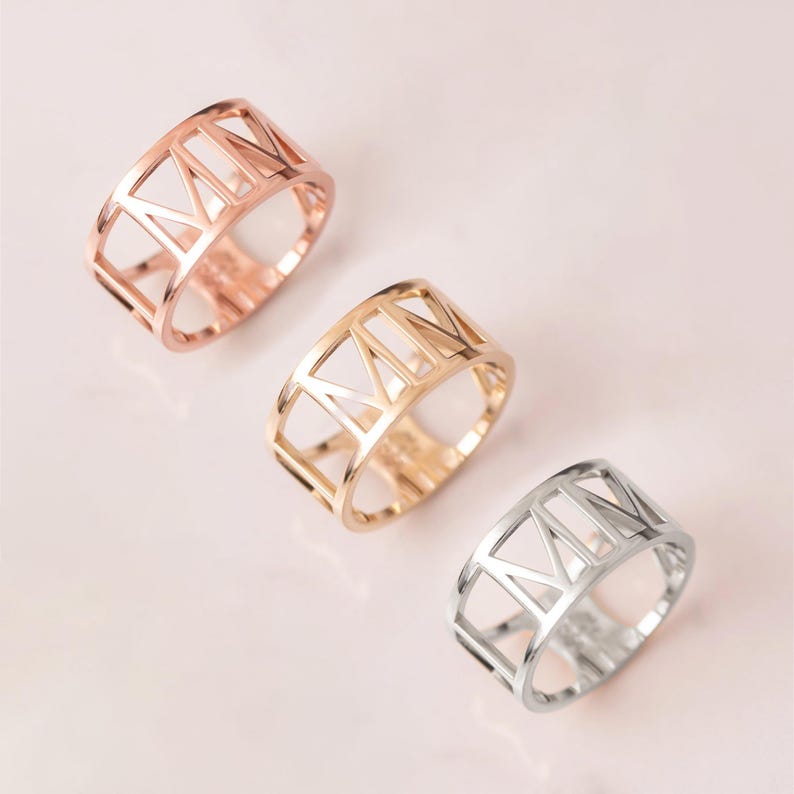 A collection of three elegant rings featuring a unique cut-out Roman numeral design, available in rose gold, yellow gold, and white gold. Each handmade piece showcases a blend of modern craftsmanship and timeless style, perfect for fashion enthusiasts or as a thoughtful gift.