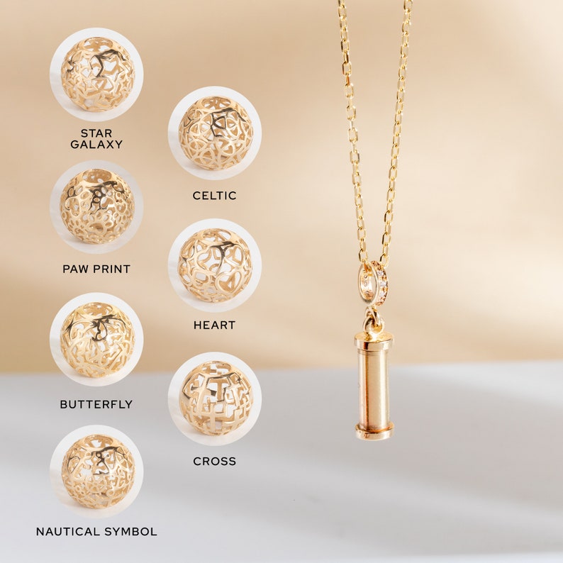 May include: A gold necklace with a cylindrical pendant and a variety of gold charms with different designs, including a star galaxy, celtic, paw print, heart, butterfly, cross, and nautical symbol.