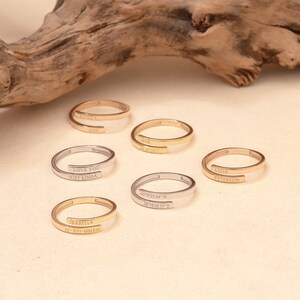 Assorted custom gold wrap rings with engraved coordinates, dates, and names in rose, yellow, and white gold.