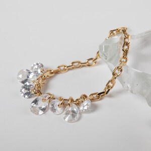 Puede incluir: Una pulsera de cadena en tono dorado que presenta una serie de cristales transparentes facetados, en forma de lágrima y redondos, que cuelgan. Los eslabones metálicos son uniformes en tamaño y forma, creando un bucle continuo de dijes.