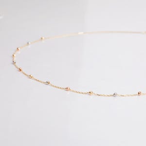 May include: A delicate gold chain necklace with small, round beads in three different colors: yellow, white, and rose gold.