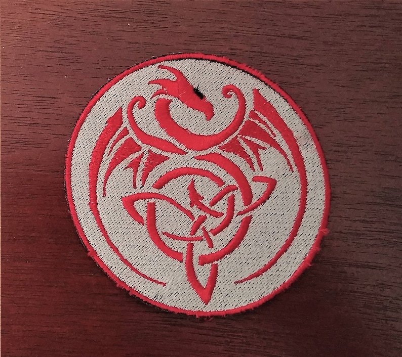 May include: A red embroidered dragon design on a white circular patch. The dragon is curled up in a knot with its wings spread out.