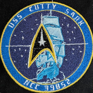 May include: A blue and gold embroidered patch with a starship and the text "USS Cutty Sark NCC-39852".