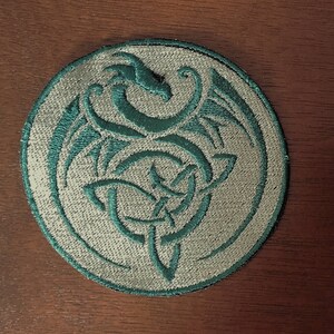 May include: A circular embroidered patch with a teal green dragon design on a white background.