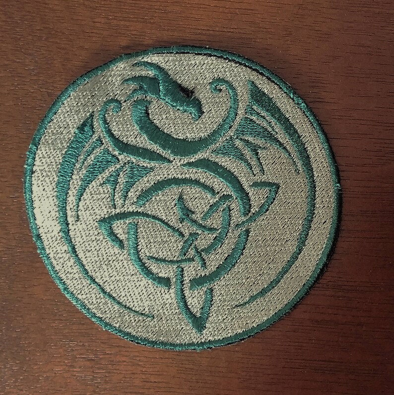 May include: A circular embroidered patch with a teal green dragon design on a white background.
