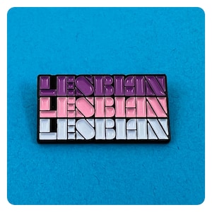 Puede incluir: Un pin de esmalte negro con la palabra "LESBIAN" repetida tres veces en un patrón geométrico. La palabra está en morado, rosa y azul claro.