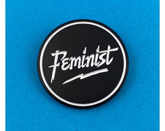 May include: Black and white enamel pin with the word "Feminist" written in a stylized font.