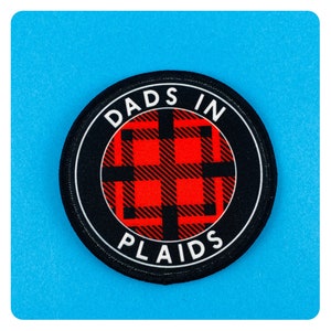May include: A black and white circular patch with the text "Dads in Plaids" in white lettering. The centre of the patch features a red and black plaid pattern.