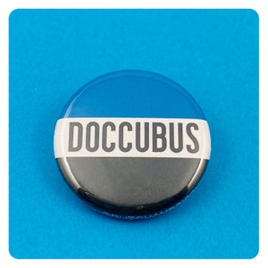 May include: A blue, white and black button with the word "DOCCUBUS" printed in white on a white stripe.