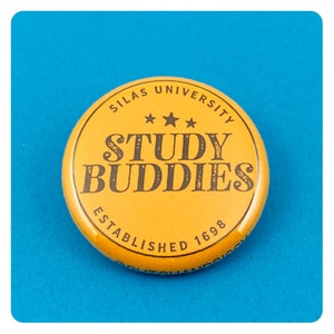 Puede incluir: Un botón amarillo con el texto "Silas University Study Buddies Established 1698" en letras negras.