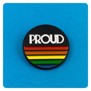 May include: A black and white button with the word "PROUD" in white letters on a black background. The button has a rainbow stripe design.