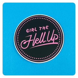 以下が含まれることがあります： 黒とピンクの丸いステッカーで、ピンクの文字で「Girl the Hell Up」と書かれています。