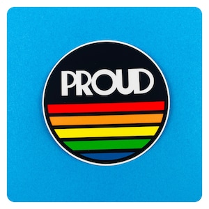 Op de afbeelding: Een zwart-witte sticker met het woord "PROUD" in witte letters op een zwarte achtergrond. De sticker heeft een regenboogstrepenontwerp met rode, oranje, gele, groene, blauwe en paarse strepen.