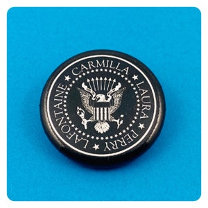 May include: Black and white button with the text "CARMILLA LAURA PERRY LAFONTAINE" around a stylized eagle with the text "E PLURIBUS UNUM" above it.