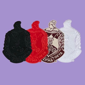 May include: Four embroidered patches in black, red, brown and white. Each patch features a shield design with the Greek letters Delta, Sigma, and Theta, along with other symbols. The patches are displayed on a purple background.