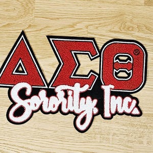 May include: A red, black, and white sorority patch with the Greek letters Delta, Sigma, and Omega, and the words "Sorority Inc." The patch is embroidered with a black border and a white outline.