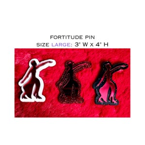May include: Three pins featuring a dancer silhouette design. The pins are red, glittery red, and black with pink accents. The text "FORTITUDE PIN" is above the pins. The pins are 7.6 cm wide and 10.2 cm high.