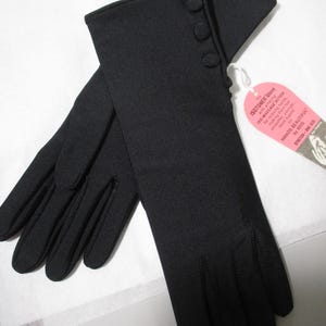 Pode incluir: Um par de luvas pretas Isotoner com tr&ecirc;s bot&otilde;es decorativos no punho. As luvas s&atilde;o feitas de um material el&aacute;stico e t&ecirc;m uma etiqueta que diz "ISOTONER Glove" e "HANDS BEAUTIFUL".