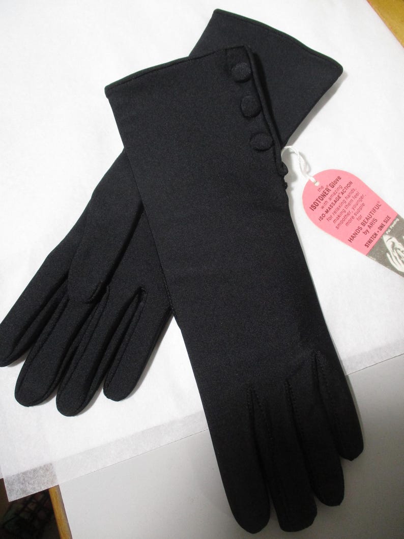 Pode incluir: Um par de luvas pretas Isotoner com tr&ecirc;s bot&otilde;es decorativos no punho. As luvas s&atilde;o feitas de um material el&aacute;stico e t&ecirc;m uma etiqueta que diz "ISOTONER Glove" e "HANDS BEAUTIFUL".