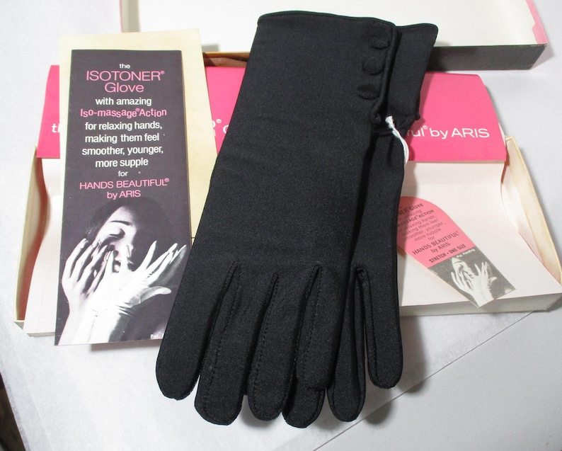 Pode incluir: Luvas Isotoner pretas com tr&ecirc;s pequenos bot&otilde;es no punho, expostas na caixa original. A caixa inclui um encarte promocional com texto sobre as luvas e a frase "Hands Beautiful".