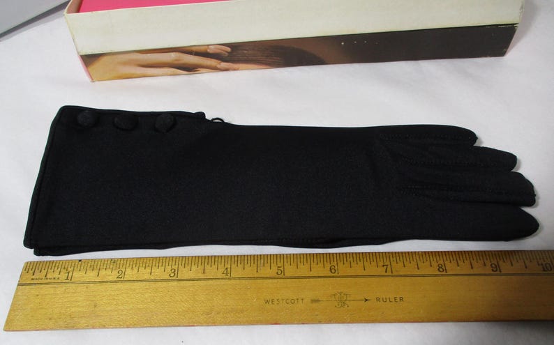Pode incluir: Uma luva preta com tr&ecirc;s bot&otilde;es decorativos no pulso. A luva tem aproximadamente 25 cm de comprimento. Uma r&eacute;gua de madeira &eacute; colocada ao lado da luva para medi&ccedil;&atilde;o.