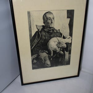 May include: Black and white framed print of a man holding a candle and a white cat, with a goat in the foreground. The artwork is in a black frame with a cream-colored mat.