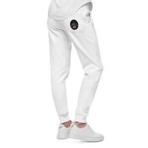 Może przedstawiać: Białe spodnie dresowe z okrągłą naszywką w kolorze czarnym i złotym na tylnej kieszeni, na której widnieje napis "Humble & Hungry".