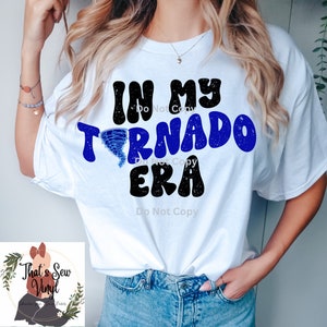 Peut inclure: T-shirt blanc avec le texte "In My Tornado Era" en lettres bleues et noires avec un graphique de tornade bleue.