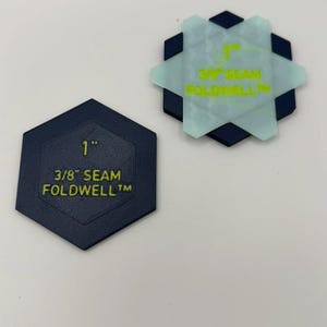 Può includere: Due strumenti da cucito esagonali etichettati 1 inch e 3/8 inch SEAM FOLDWELL. Uno è blu scuro solido, l'altro è blu chiaro traslucido sovrapposto a un esagono blu scuro. Entrambi presentano testo giallo che indica le misure del margine di cucitura.
