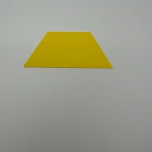 Könnte beinhalten: Eine flache, gelbe, zweidimensionale Trapezform, die aus einem dünnen Material ausgeschnitten ist. Das Objekt hat eine breite Basis, eine kürzere parallele Oberkante und zwei gleich lange, schräge Seiten, die eine geometrische Form bilden.