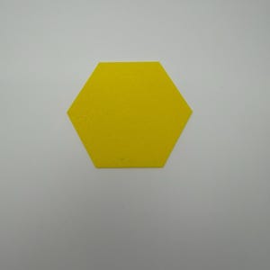 Könnte beinhalten: Ein leuchtend gelbes Sechseck mit einer strukturierten Oberfläche. Die Form weist sechs gleich lange Seiten und sechs Winkel auf und wirkt flach und einheitlich. Das Material zeigt ein feines, subtiles Muster auf der gelben Fläche.