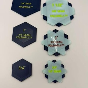 Könnte beinhalten: Ein Set aus dunkelblauen, sechseckigen Quilt-Schablonen mit der Beschriftung 1 1/2 inch, 1 inch und 3/4 inch sowie 3/8 inch Nahtzugabe, kombiniert mit durchscheinenden, hellblauen sternförmigen Auflagehilfen mit passendem Text.